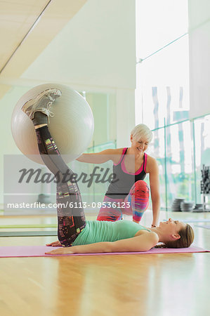 Personal trainer guiding woman with fitness ball between legs