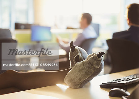 Businesswoman wearing wolf paw slippers with feet up on office desk
