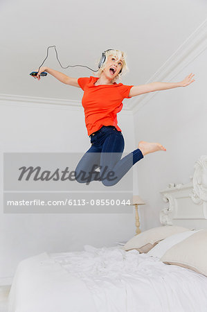 Playful woman jumping on bed listening to music with headphones and mp3 player