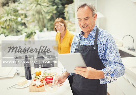 Mature couple with digital tablet cooking in kitchen