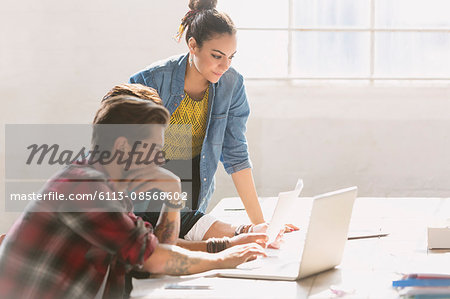 Creative young business people working at laptop in sunny office