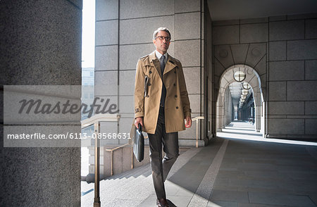 Corporate businessman in trench coat walking in cloister
