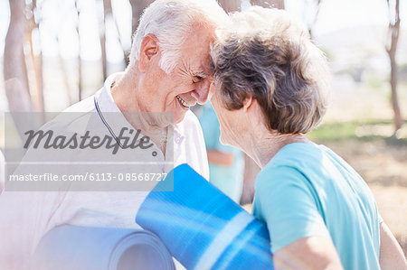 Affectionate senior couple holding yoga mats in park