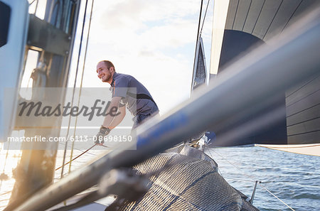 Smiling man sailing holding rigging on sailboat