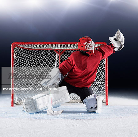Hockey goalie in red uniform reaching for puck with glove at goal net