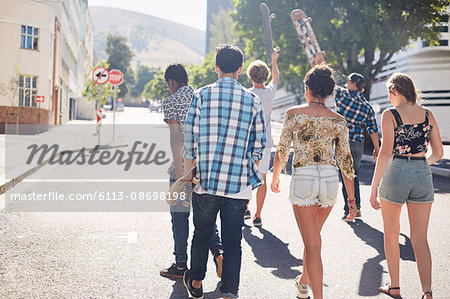 Teenage friends with skateboards walking on sunny urban street