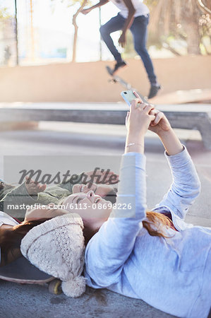 Teenage girls laying taking selfie with camera phone at skate park