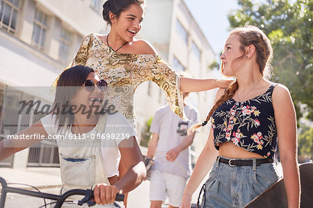 Teenage girls with BMX bicycle and skateboard on sunny urban street
