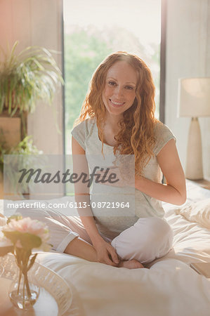 Portrait smiling pregnant woman sitting on bed