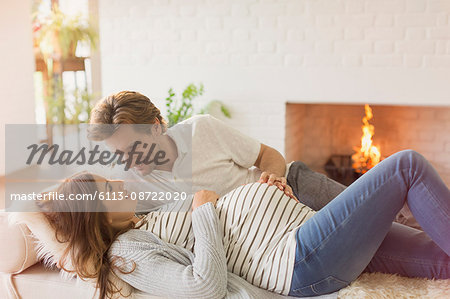 Pregnant couple laying and talking near fireplace in living room