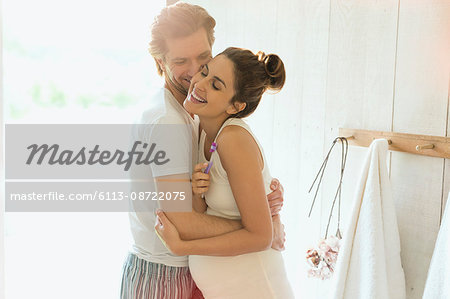 Affectionate pregnant couple hugging in sunny bathroom