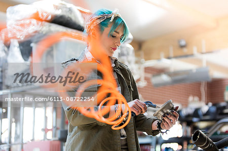 Young female mechanic with blue hair using equipment in auto repair shop