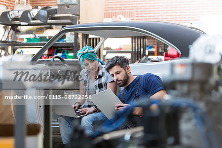 Mechanics working with clipboard and laptop in auto repair shop