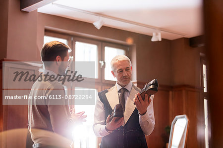 Businessman being fitted for suit examining dress shoes in menswear shop