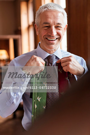Smiling businessman trying on ties in mirror at menswear shop