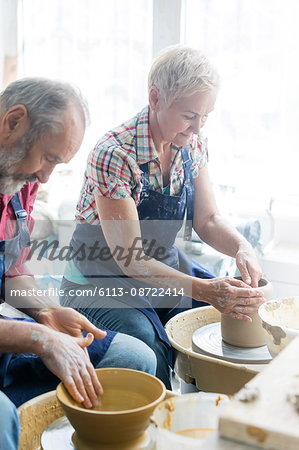 Senior couple using pottery wheels in studio