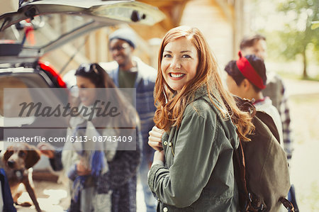 Portrait smiling hiker holding backpack with friends at back of car