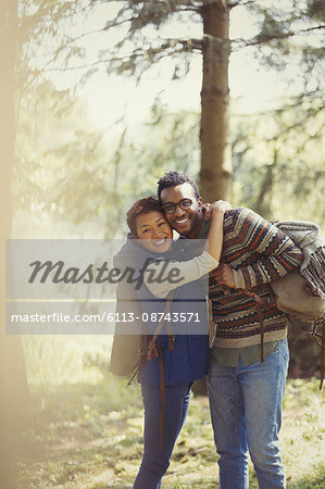 Portrait smiling couple with backpacks hiking in woods