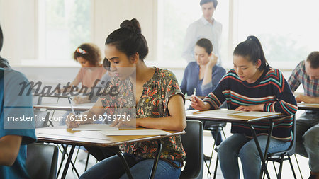 College Students Taking Test At Desks In Classroom Stock Photo