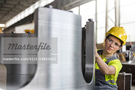 Female steel worker examining steel part in factory