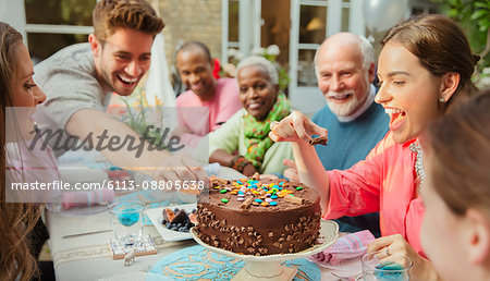 Family reaching for candy on chocolate birthday cake at patio table