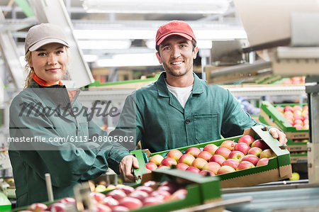 Portrait smiling workers with boxes of red apples in food processing plant