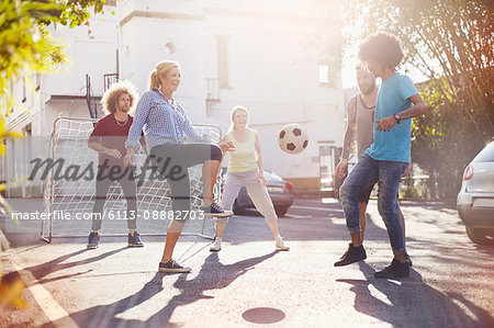 Friends playing soccer in sunny summer street