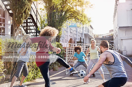 Friends playing soccer in sunny summer street