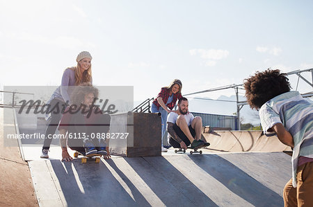 Friends pushing each other on skateboards at sunny skate park