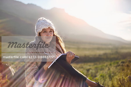 Young woman writing in journal in sunny, remote field