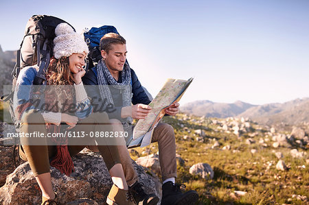 Young couple with backpacks hiking, resting and checking map on sunny rocks Young couple with backpacks hiking, resting and checking map on sunny rocks