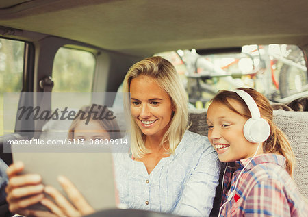 Mother and daughters watching video on digital tablet in back seat of car