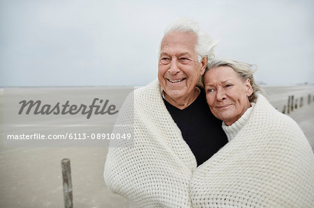 Smiling affectionate senior couple wrapped in a blanket on beach