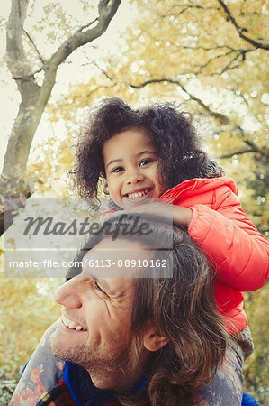 Portrait smiling father father carrying daughter on shoulders in autumn park