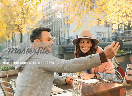 Young couple taking selfie with camera phone at autumn sidewalk cafe