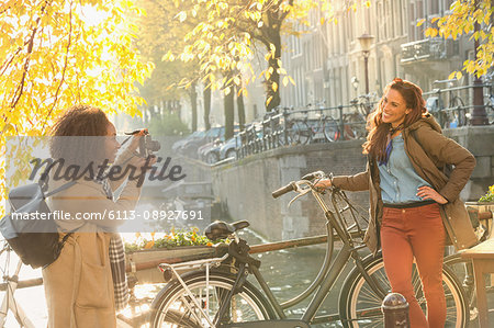Young woman photographing friend with bicycle along autumn canal, Amsterdam