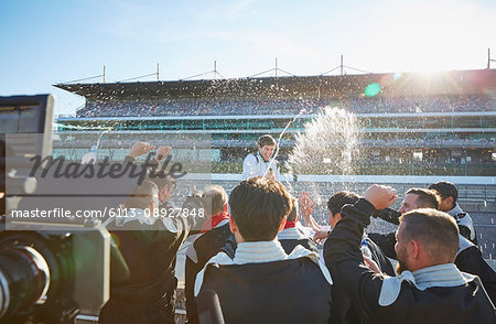 Formula one racing team spraying champagne on driver, celebrating victory on sports track