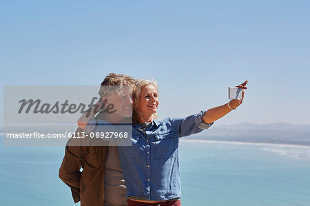 Affectionate senior couple taking selfie overlooking sunny ocean view