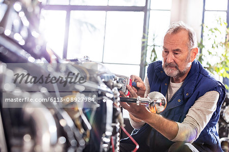 Senior male motorcycle mechanic fixing motorcycle in workshop