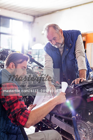 Male motorcycle mechanics reviewing plans in workshop