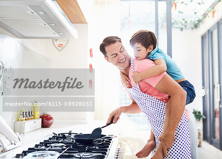Father piggybacking son, cooking at stove in kitchen
