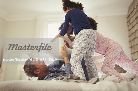 Playful multi-ethic father and daughters pillow fighting on bed