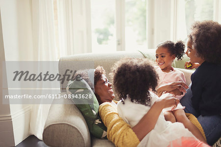 Affectionate daughters cuddling mother laying on sofa