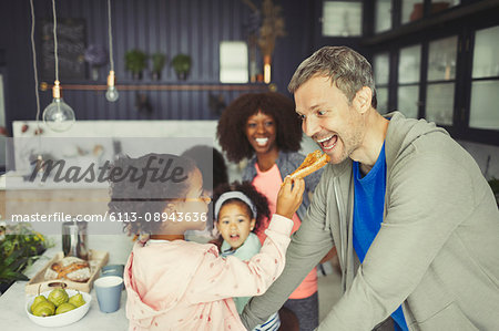 Multi-ethnic daughter feeding toast to father in kitchen