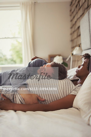 Affectionate pregnant couple cuddling and napping on bed