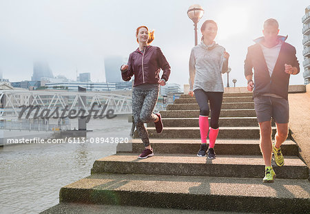 Runners running down steps along sunny urban waterfront