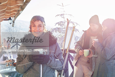Portrait smiling female skier drinking coffee on cabin deck with friends apres-ski
