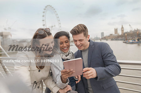 Friend tourists using digital tablet on bridge over Thames River, London, UK