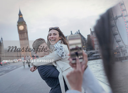 Playful couple tourists being photographed on bridge near Big Ben, London, UK