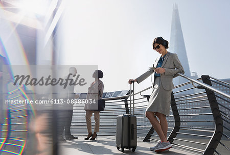 Businesswoman with suitcase listening to music with smart phone and headphones, London, UK